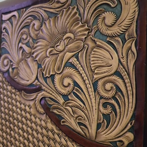 Puede incluir: Un primer plano de un panel de cuero con intrincados diseños cincelados. El panel presenta un motivo floral con una gran flor en el centro, rodeada de enredaderas y hojas que se arremolinan. El fondo es de color azul oscuro y el cuero es de color marrón claro.