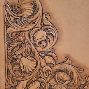 Puede incluir: Primer plano de una superficie de cuero marrón con un diseño floral detallado tallado en ella. El diseño presenta intrincados remolinos, hojas y flores.
