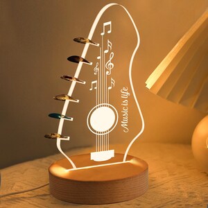 Pu&ograve; includere: Lampada a LED a forma di chitarra con la scritta "Music is life". La lampada presenta una base in legno e un design a chitarra in acrilico trasparente con note musicali e plettri. La lampada emette una calda luce, ideale per gli amanti della musica.