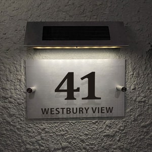 May include: A silver house number sign with the number 41 and the text "WESTBURY VIEW" in black lettering. The sign is illuminated by a solar-powered light fixture above it.