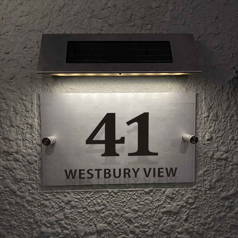 May include: A silver house number sign with the number 41 and the text "WESTBURY VIEW" in black lettering. The sign is illuminated by a solar-powered light fixture above it.