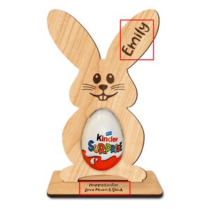 Op de afbeelding: Een houten paas konijnenstandaard met een gleuf voor een chocolade-ei. Het konijn heeft een glimlachend gezicht en de woorden "Prettige Pasen Liefs Mama & Papa" staan op de basis. Het konijn is gepersonaliseerd met de naam "Emily" op het oor.