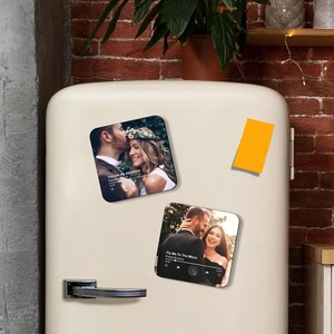 May include: Two square magnets with romantic photos of couples. One magnet features a couple with the text "You are my sunshine" and the other has the text "Fly Me To The Moon". The magnets are on a white refrigerator.
