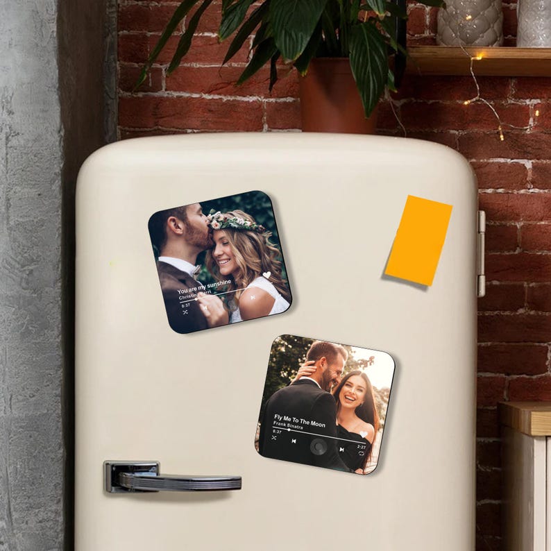 May include: Two square magnets with romantic photos of couples. One magnet features a couple with the text "You are my sunshine" and the other has the text "Fly Me To The Moon". The magnets are on a white refrigerator.