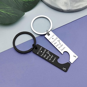 May include: Two keyrings with bottle opener features. One is black, the other is silver. Both have the text "You hold the key to my heart" and the date 02.11.2025. Each keyring has the letter "S".
