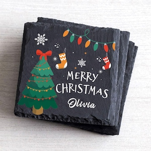 May include: Black slate coasters featuring a Christmas tree, lights, stockings, snowflakes, and the text "Merry Christmas Olivia".
