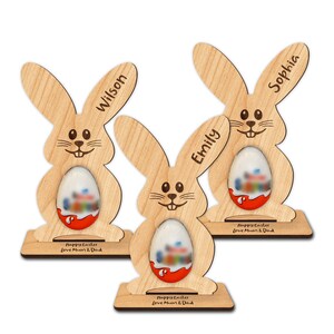 Op de afbeelding: Drie houten paashazen-eierhouders met gepersonaliseerde namen "Wilson", "Emily" en "Sophia". Elke houder heeft een gleuf voor een chocolade-ei en een voet met de tekst "Prettige Pasen Liefs Mama en Papa".