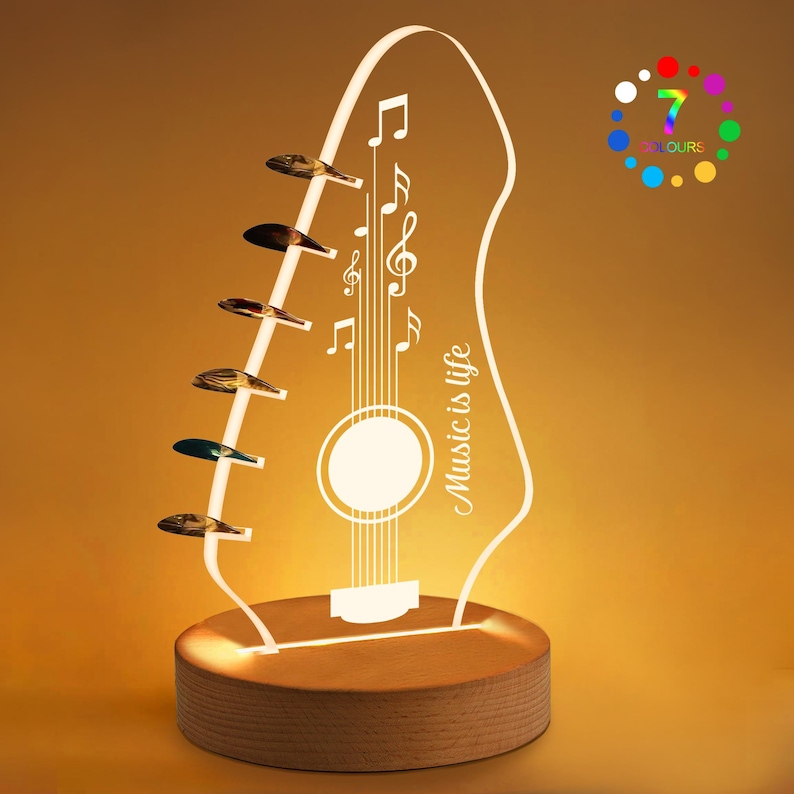Pu&ograve; includere: Lampada a LED a forma di chitarra con base in legno. La lampada presenta un contorno bianco di una chitarra con note musicali e la scritta "Music is life". Sette plettri sono attaccati al lato. La lampada ha una funzione di cambio colore.