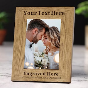 May include: A wooden picture frame with a light brown finish. The frame has a space for a photo and a space for an engraved message. The message says "Your Text Here" and "Engraved Here Personalised for Any Occasion".