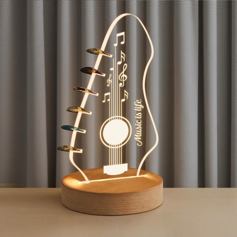 Pu&ograve; includere: Lampada a LED a forma di chitarra con base in legno. La lampada presenta note musicali e la scritta "Music is life". La paletta della chitarra ha pioli decorativi. La lampada emette una calda luce, ideale per gli amanti della musica.