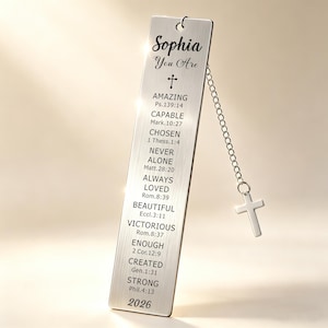 May include: A silver bookmark with the name "Sophia" and the words "You Are" above a cross symbol. The bookmark has a chain with a small cross charm. The bookmark also has inspirational words and Bible verses.