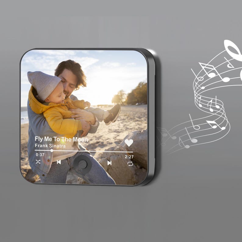 May include: A black square music player displays a photo of a person holding a child. The screen shows the song "Fly Me To The Moon" by Frank Sinatra. White musical notes are on the right side of the player.