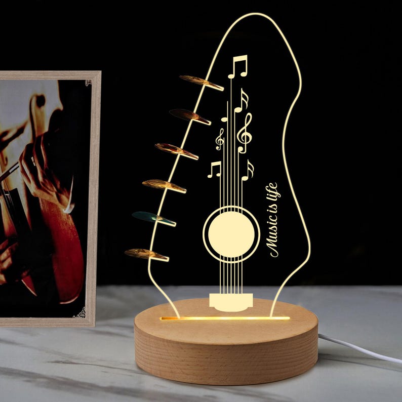Pu&ograve; includere: Lampada decorativa a forma di chitarra con la scritta "Music is life". La lampada presenta note musicali e una base in legno. La lampada &egrave; illuminata da una luce calda e soffusa.