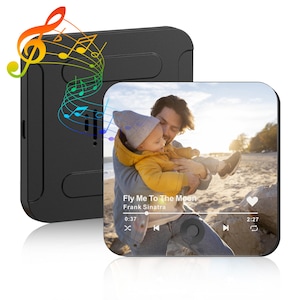 May include: Black square music player with a screen displaying a photo of a person holding a baby. The screen shows the song "Fly Me To The Moon" by Frank Sinatra. Colorful musical notes emanate from the player.