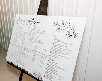 May include: A white board with a crossword puzzle and a list of questions for a wedding game. The board has the names Jon & Allison and the date October 10, 2023.