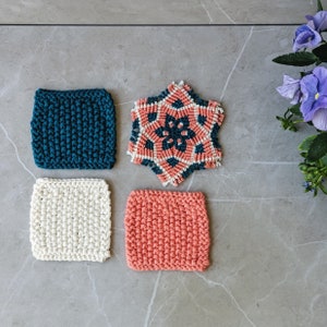 May include: Four handmade coasters in various colors and designs. Includes a teal square coaster, a white square coaster, a coral square coaster, and a star-shaped coaster with coral, teal, and white accents. The coasters are made of a textured, knitted material.