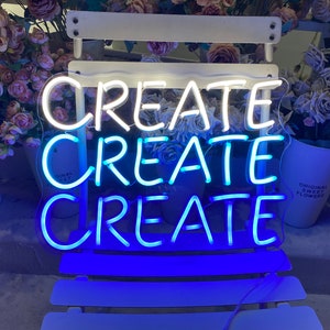 Puede incluir: Un letrero de neón con la palabra "CREATE" repetida tres veces. Las dos primeras palabras están en neón blanco, y la última palabra está en neón azul.