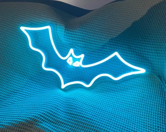 May include: A white neon bat sign with a blue glow, hanging on a blue textured background.