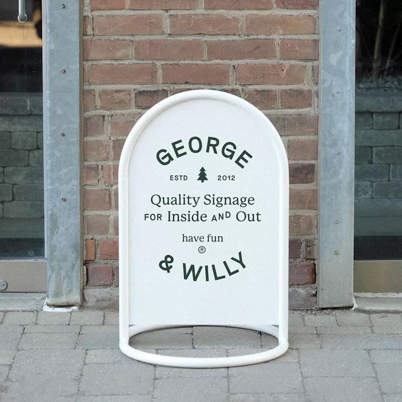 May include: A white, arched sidewalk sign with black text. The sign reads "GEORGE ESTD 2012 Quality Signage FOR Inside AND Out have fun & WILLY". The sign has a rounded base and a metal frame.
