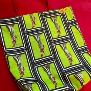 May include: A green tote bag with a repeating pattern of legs in black and white striped stockings and red high heels. The bag has a red handle and a small tag that reads "Pushing Up Wildflowers".