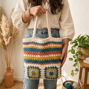 Peut inclure: Un sac fourre-tout en crochet crème avec un motif rayé coloré en bleu sarcelle, corail et jaune. Le sac présente deux motifs floraux carrés en bas et des anses crème.