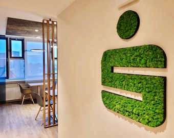 May include: A green moss wall art piece in the shape of the letter "S" with a smaller circle of moss above it. The art is mounted on a white wall in an office setting.