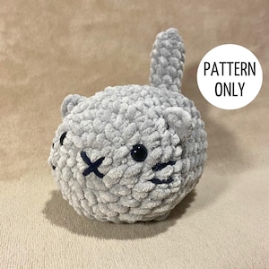 以下が含まれることがあります： 黒い刺繍の目と縫い付けられた口が付いた、グレーの毛糸で編まれた猫のぬいぐるみ。おもちゃは丸い体と長い尻尾を持つ猫の形をしています。