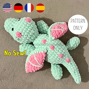 May include: A crochet pattern for a no-sew dragon amigurumi toy. The dragon is green with pink wings and a white outline. The pattern is available for purchase.