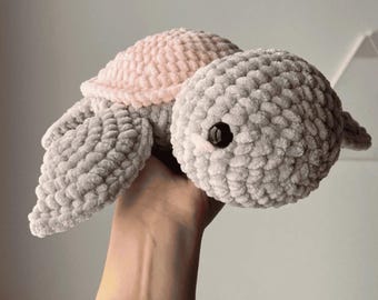 May include: A crocheted plush toy turtle with a pink shell and gray body. The turtle has black eyes and a soft, fuzzy texture.