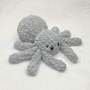Op de afbeelding: Een gehaakte grijze octopus knuffel. Het zachte speelgoed heeft een afgeronde kop en lichaam, met acht lange, getextureerde tentakels die naar buiten uitsteken. De octopus heeft kleine, donkere ogen. Het speelgoed is gemaakt van een zacht, pluizig materiaal.
