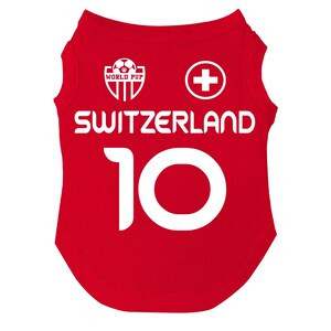 Puede incluir: Camiseta roja para perro con la palabra "SWITZERLAND" en blanco y el n&uacute;mero "10". La camiseta tambi&eacute;n presenta una cruz suiza blanca y un logotipo de "WORLD PUP".