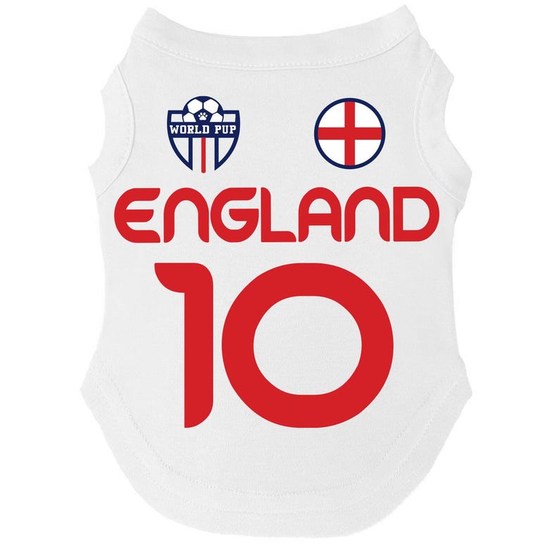 Puede incluir: Camiseta blanca para perro con la palabra "ENGLAND" en letras rojas y el n&uacute;mero "10". La camiseta tiene un escudo azul y blanco que dice "WORLD PUP" y una cruz roja sobre un c&iacute;rculo blanco.