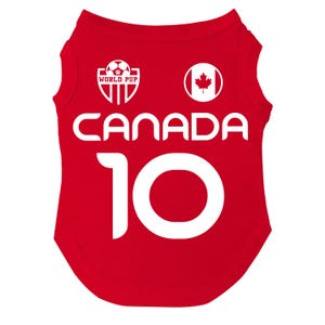 Puede incluir: Camiseta roja para perro con texto y gr&aacute;ficos blancos. La camiseta presenta la palabra "CANADA" y el n&uacute;mero "10". Incluye una bandera canadiense y un logotipo de "WORLD PUP" con un bal&oacute;n de f&uacute;tbol.