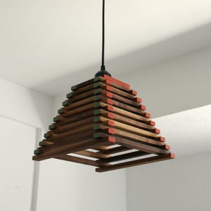 Puede incluir: Una lámpara colgante de madera con forma de pirámide. La luz está hecha de múltiples capas de madera, con acentos verdes y rojos alternos.