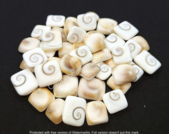 May include: A pile of white and brown square shaped shell cabochons with a spiral pattern.