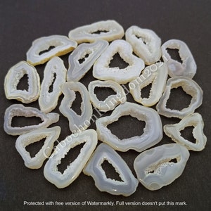 Puede incluir: Una colección de rodajas de ágata blanca con una abertura de cueva de cristal natural en el centro. Las rodajas son de varias formas y tamaños, algunas son más ovaladas y otras más triangulares.