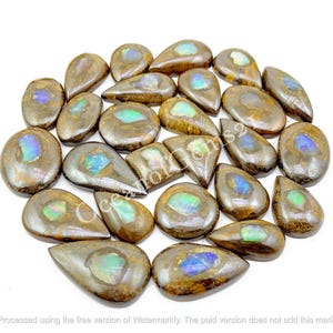 Puede incluir: Una colección de piedras preciosas pulidas, de forma ovalada, con una matriz marrón e inclusiones iridiscentes y coloridas. Las piedras preciosas varían en tamaño y forma, con una mezcla de formas de lágrima y redondeadas. La paleta de colores incluye marrones, azules y verdes.