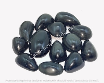 Könnte beinhalten: Eine Ansammlung polierter, schwarzer Obsidiansteine in verschiedenen Formen, darunter oval und tropfenförmig. Die Steine haben eine glänzende, reflektierende Oberfläche. Das Bild enthält den Text "Cabochon Kingdo 121".
