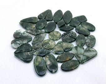 May include: A collection of green and white agate gemstone cabochons in various shapes and sizes. The cabochons are arranged in a circular pattern on a white surface.