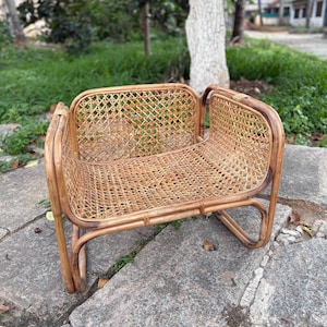 May include: A handcrafted, natural rattan chair with a woven seat and back. The chair has a curved design with rounded armrests and legs. The chair is made of light brown rattan and is suitable for indoor or outdoor use.