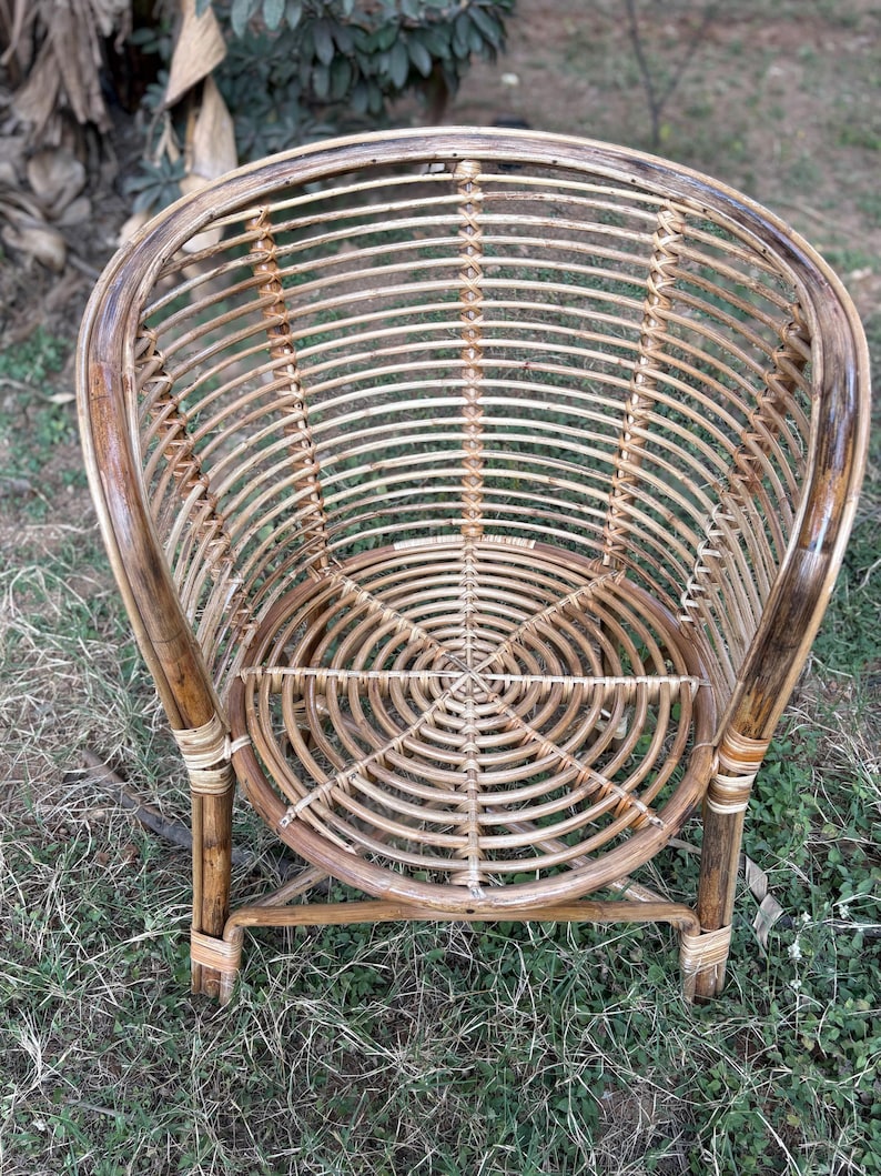 K&ouml;nnte beinhalten: Ein geflochtener Rattanstuhl mit einem runden Sitz und einer abgerundeten R&uuml;ckenlehne. Der Stuhl ist aus nat&uuml;rlichem braunem Rattan gefertigt und hat ein schlichtes, elegantes Design.