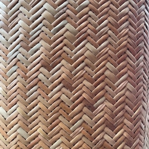 May include: Close-up of a woven basket made from natural materials. The basket has a herringbone pattern and is a light brown colour.