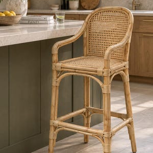 May include: A light brown rattan bar stool with a curved backrest and seat featuring a woven cane pattern. The stool has four legs connected by horizontal support bars and integrated armrests, constructed from natural bamboo-like material.