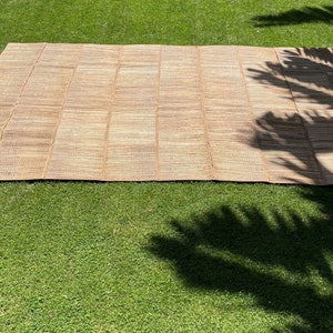 May include: A large, woven, tan-colored mat made of natural fibers. The mat is laid out on a green grassy lawn.