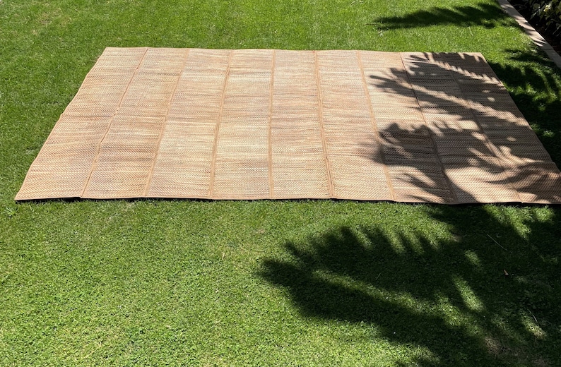 May include: A large, woven, tan-colored mat made of natural fibers. The mat is laid out on a green grassy lawn.