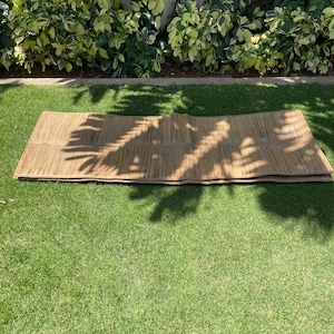 May include: A brown woven mat made of natural materials, folded in half and lying on a green grassy lawn.