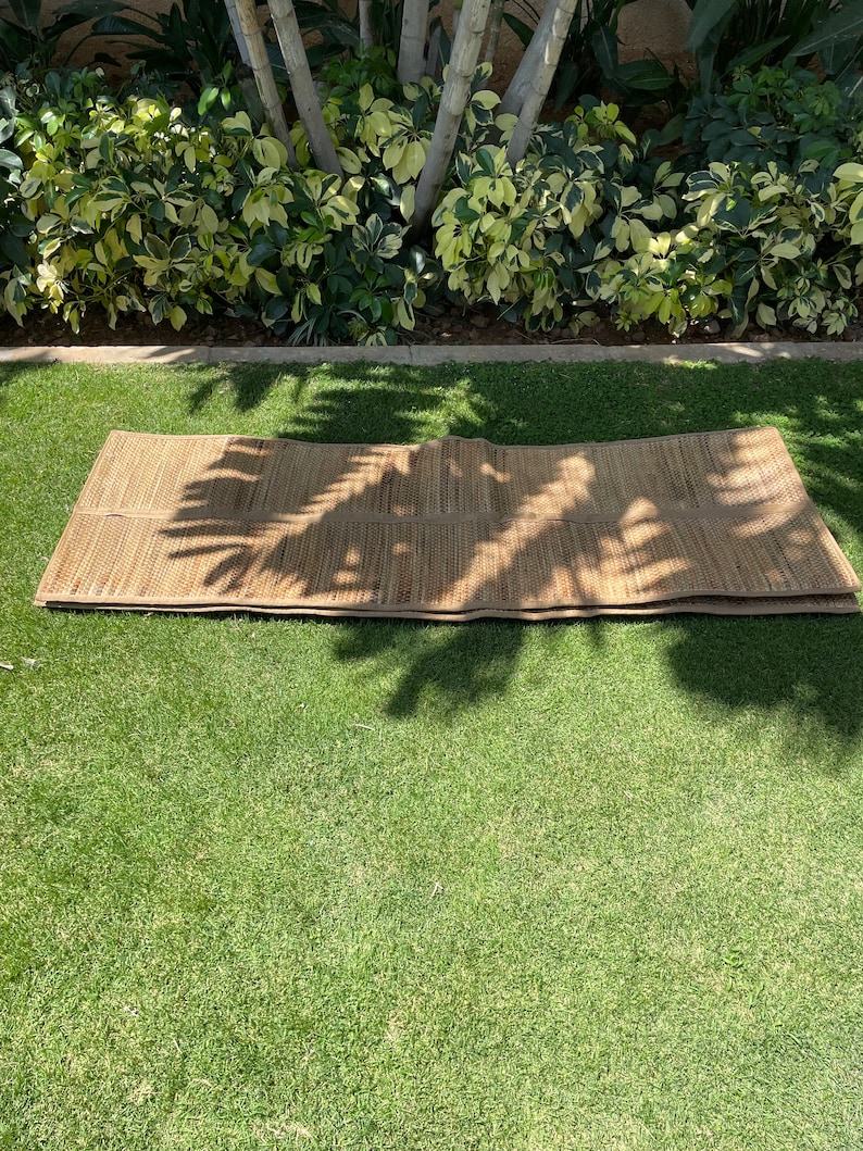 May include: A brown woven mat made of natural materials, folded in half and lying on a green grassy lawn.