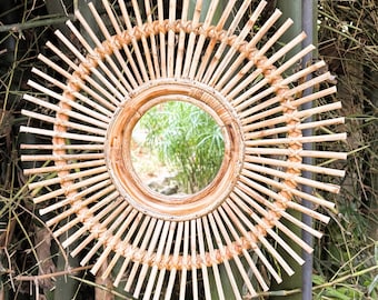 May include: A round, natural woven bamboo mirror with a sunburst design. The mirror has a natural wood frame and a clear glass reflection.