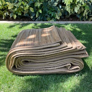 May include: A rolled up tan and brown woven mat with a stitched edge. The mat is sitting on a green grassy surface.