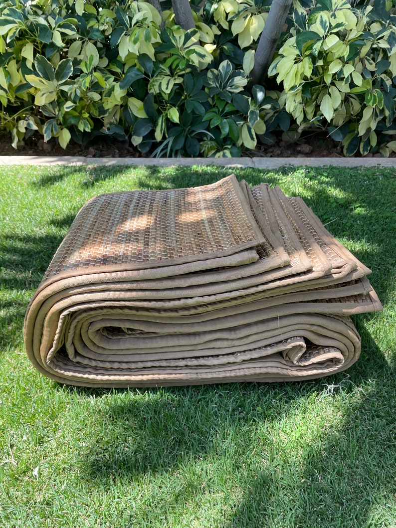 May include: A rolled up tan and brown woven mat with a stitched edge. The mat is sitting on a green grassy surface.